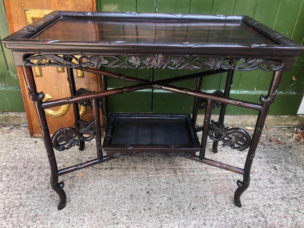 A late Qing dynasty dark carved hardwood tray table featuring faux-bamboo legs, carved foliage aprons, and a lower tier shelf.