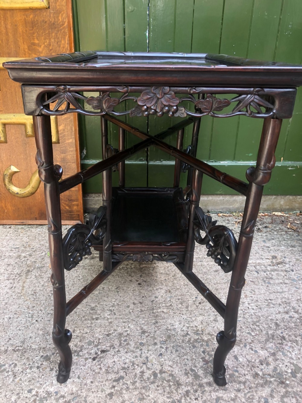 A late Qing dynasty dark carved hardwood tray table featuring faux-bamboo legs, carved foliage aprons, and a lower tier shelf. View X