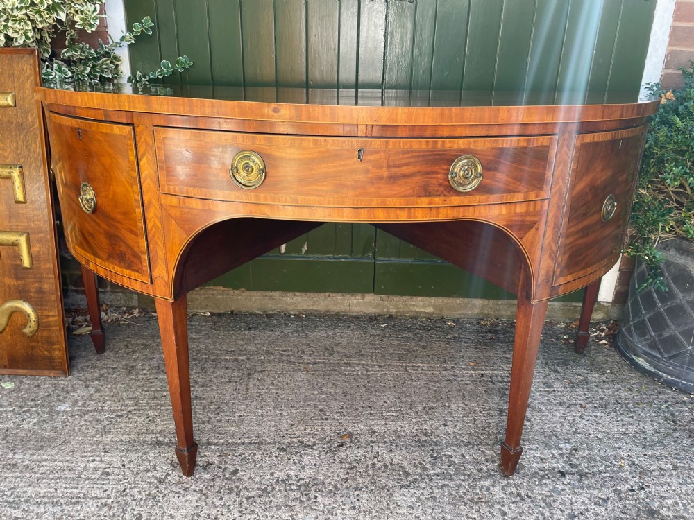 A late 18th-century George III mahogany demi-lune sideboard featuring inlaid stringing, a central drawer, curved side doors, and tapered square legs.