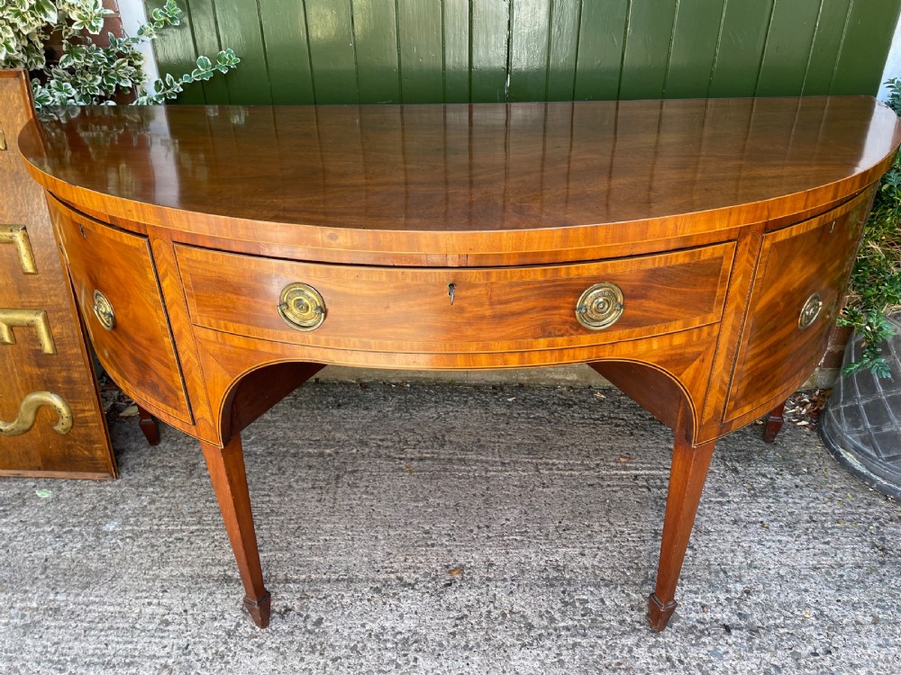 A late 18th-century George III mahogany demi-lune sideboard featuring inlaid stringing, a central drawer, curved side doors, and tapered square legs. View II