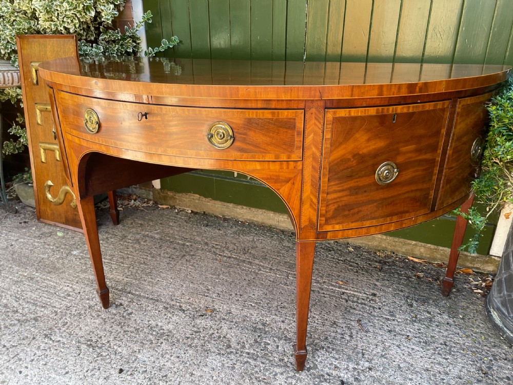 A late 18th-century George III mahogany demi-lune sideboard featuring inlaid stringing, a central drawer, curved side doors, and tapered square legs. View VI