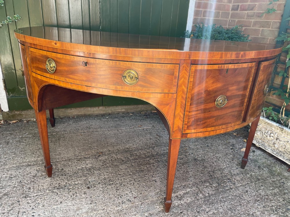 A late 18th-century George III mahogany demi-lune sideboard featuring inlaid stringing, a central drawer, curved side doors, and tapered square legs. View XII