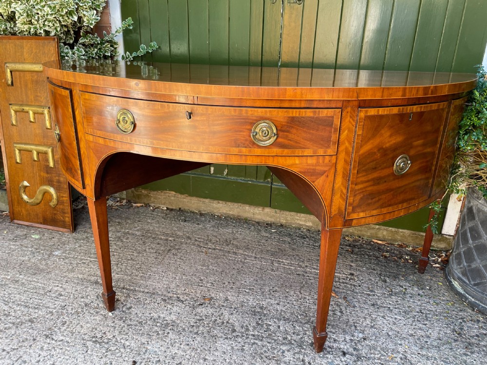 A late 18th-century George III mahogany demi-lune sideboard featuring inlaid stringing, a central drawer, curved side doors, and tapered square legs. View XVI