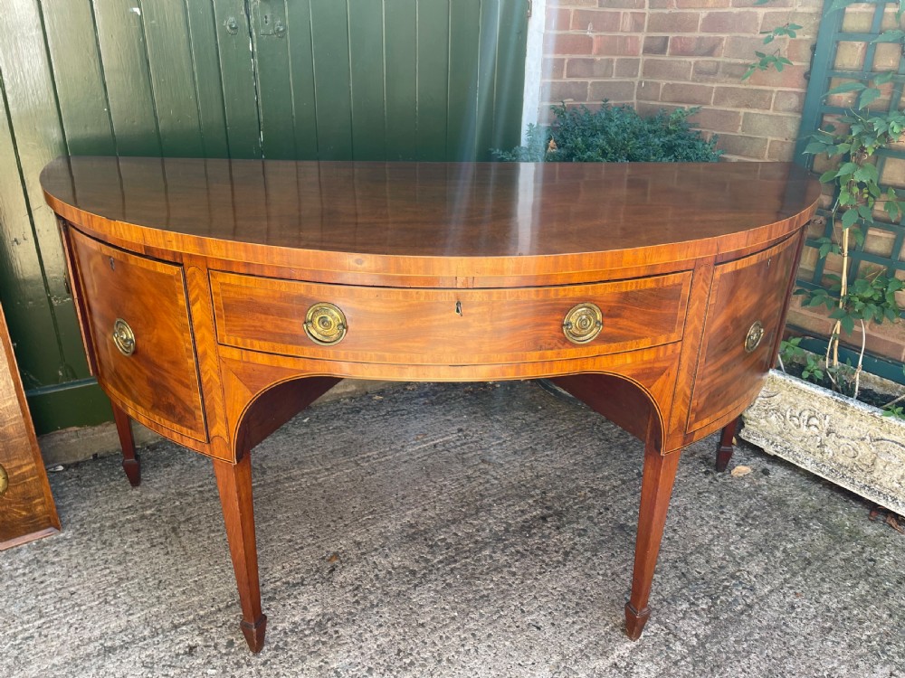A late 18th-century George III mahogany demi-lune sideboard featuring inlaid stringing, a central drawer, curved side doors, and tapered square legs. View XVII