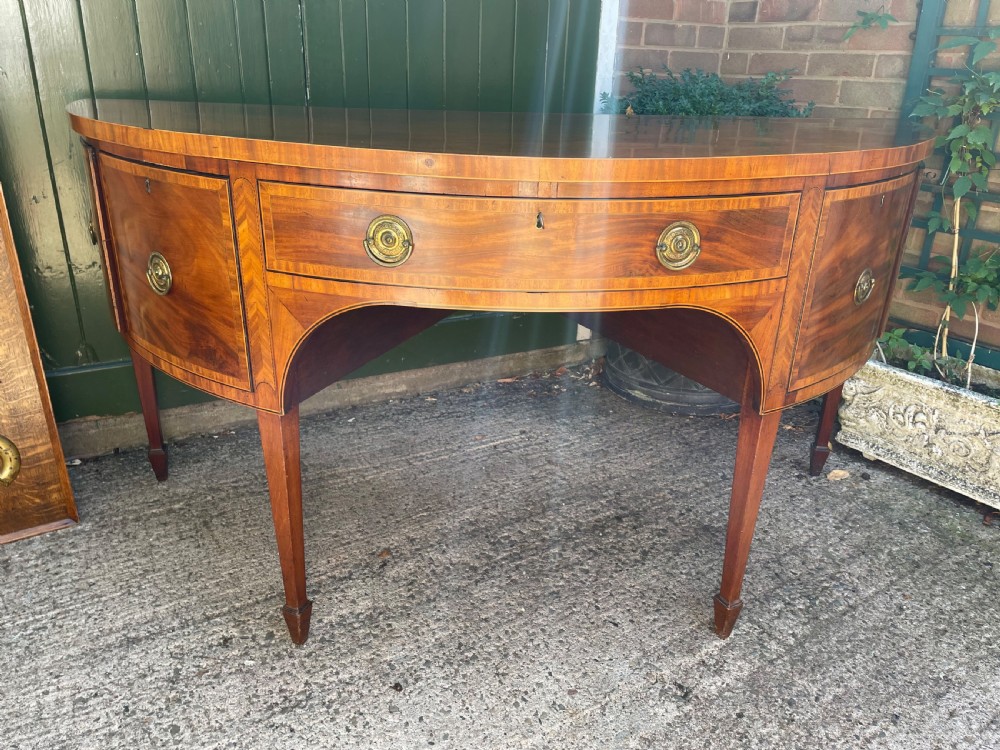 A late 18th-century George III mahogany demi-lune sideboard featuring inlaid stringing, a central drawer, curved side doors, and tapered square legs. View XVIII