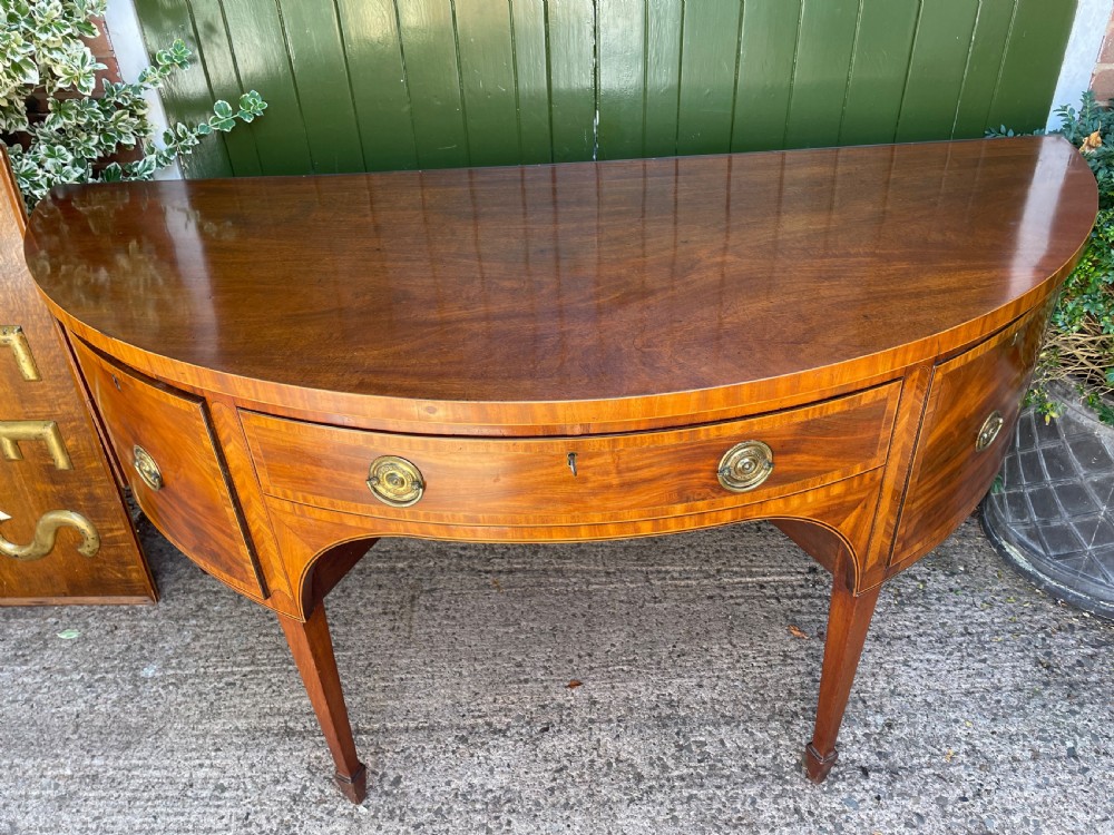 A late 18th-century George III mahogany demi-lune sideboard featuring inlaid stringing, a central drawer, curved side doors, and tapered square legs. View XIX
