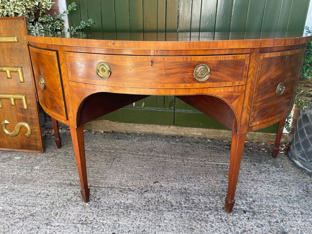 A late 18th-century George III mahogany demi-lune sideboard featuring inlaid stringing, a central drawer, curved side doors, and tapered square legs. View XXII