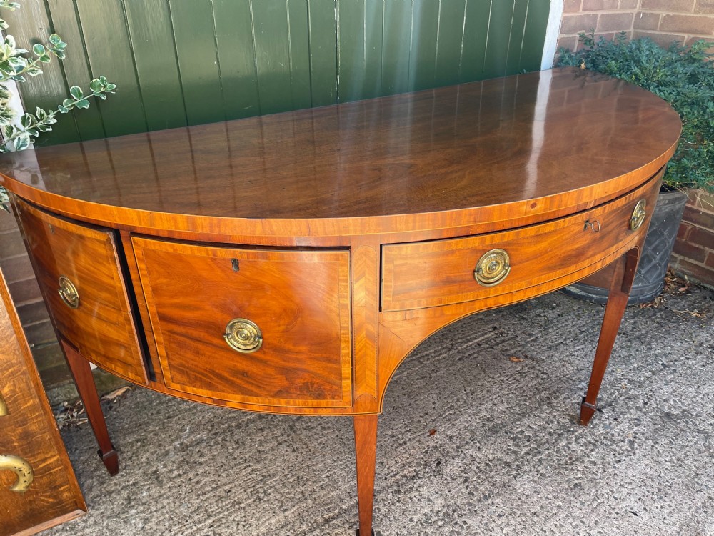 A late 18th-century George III mahogany demi-lune sideboard featuring inlaid stringing, a central drawer, curved side doors, and tapered square legs. View XXIV