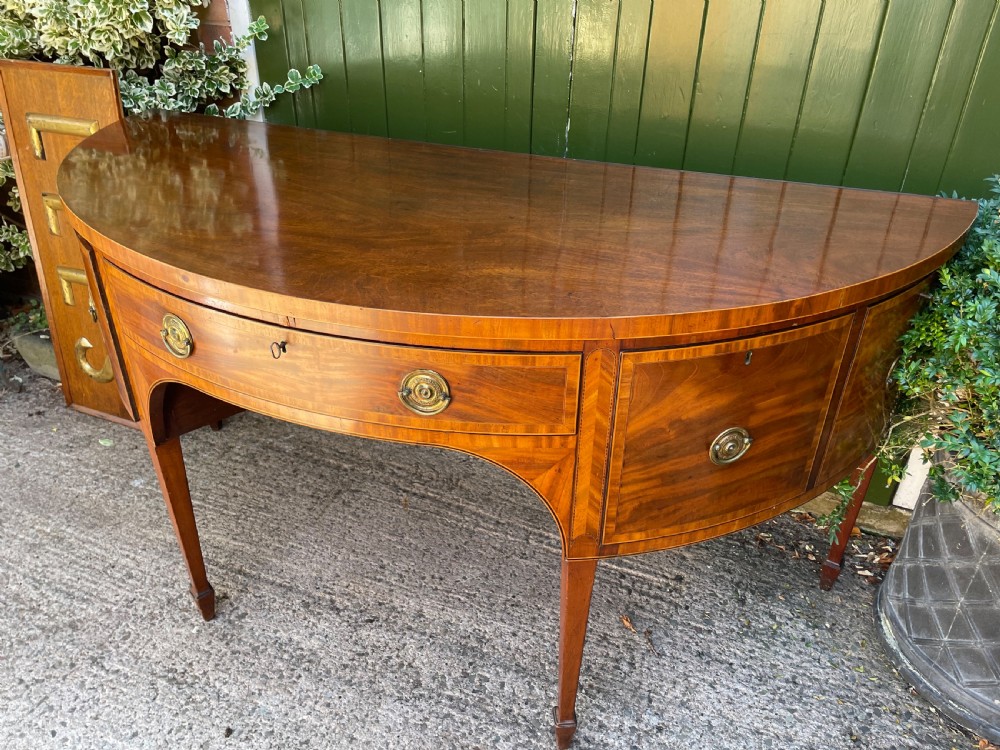 A late 18th-century George III mahogany demi-lune sideboard featuring inlaid stringing, a central drawer, curved side doors, and tapered square legs. View XXV