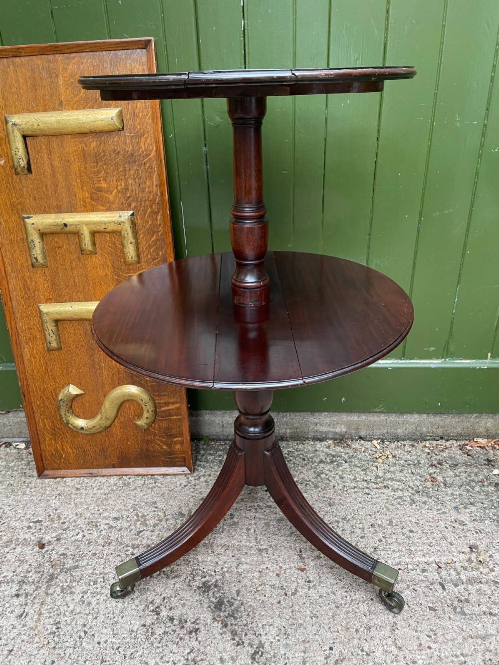 A late eighteenth-century George III mahogany two-tiered dumb waiter featuring drop-leaf circular shelves and a turned column on a tripod base with brass castors.