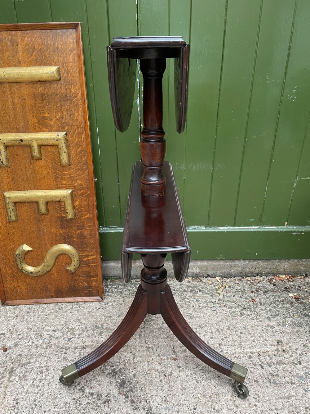 A late eighteenth-century George III mahogany two-tiered dumb waiter featuring drop-leaf circular shelves and a turned column on a tripod base with brass castors. View V