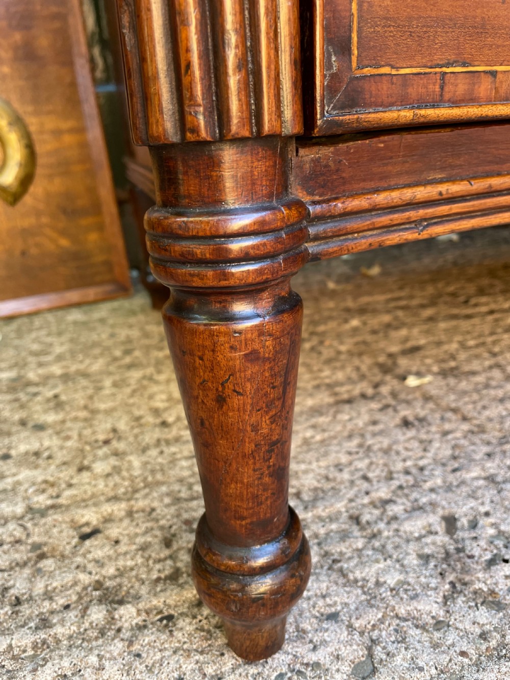 A George III Sheraton period mahogany chest of drawers featuring a curved serpentine front, four graduated drawers, brass swan-neck handles, and reeded corner columns. View XIV