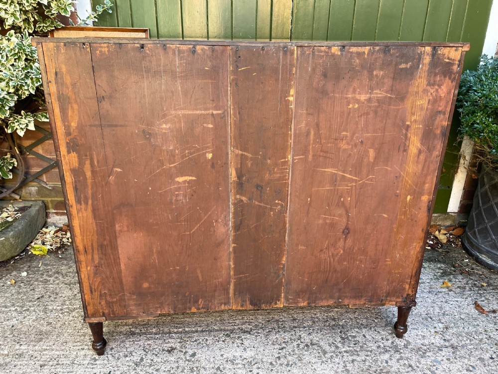 A George III Sheraton period mahogany chest of drawers featuring a curved serpentine front, four graduated drawers, brass swan-neck handles, and reeded corner columns. View XX