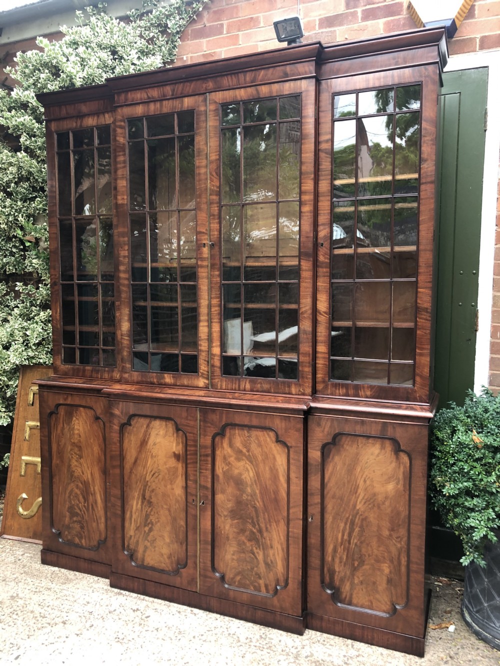 An early 19th-century George IV flame mahogany breakfront library bookcase featuring four upper glazed doors with astragal glazing bars above four fielded panel lower cupboards.