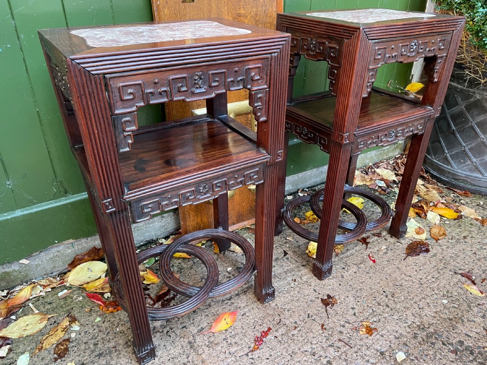 A pair of late nineteenth-century Chinese carved dark hardwood two-tier stands featuring inset marble tops, carved openwork aprons, and interlocking ring stretchers. View XX