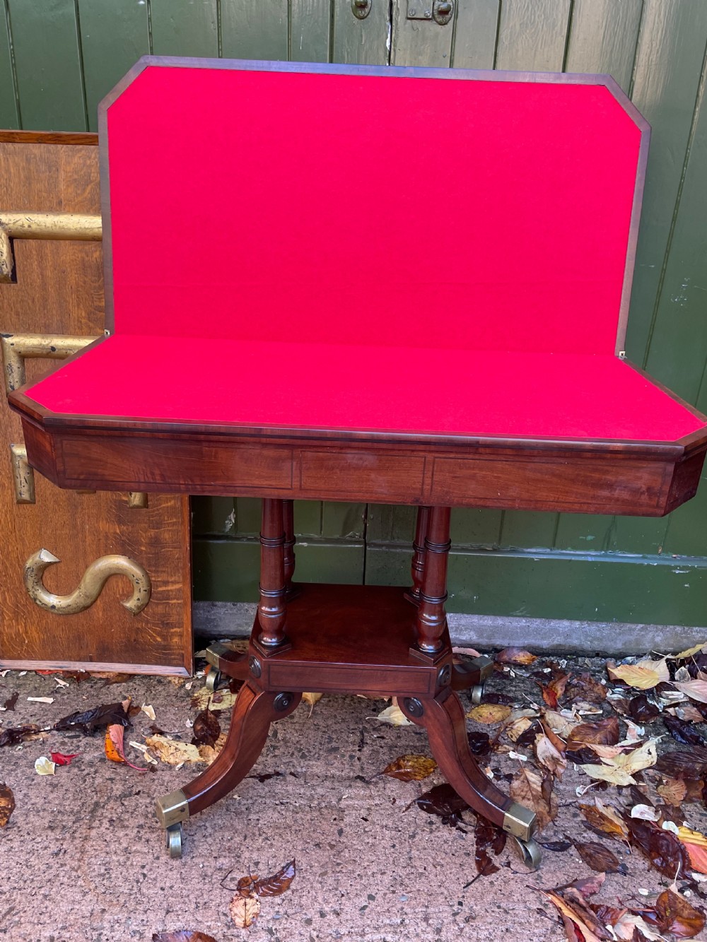 An early 19th-century Regency mahogany fold-over card table featuring turned column supports, a square platform base, and four splayed sabre legs with brass castors. View V