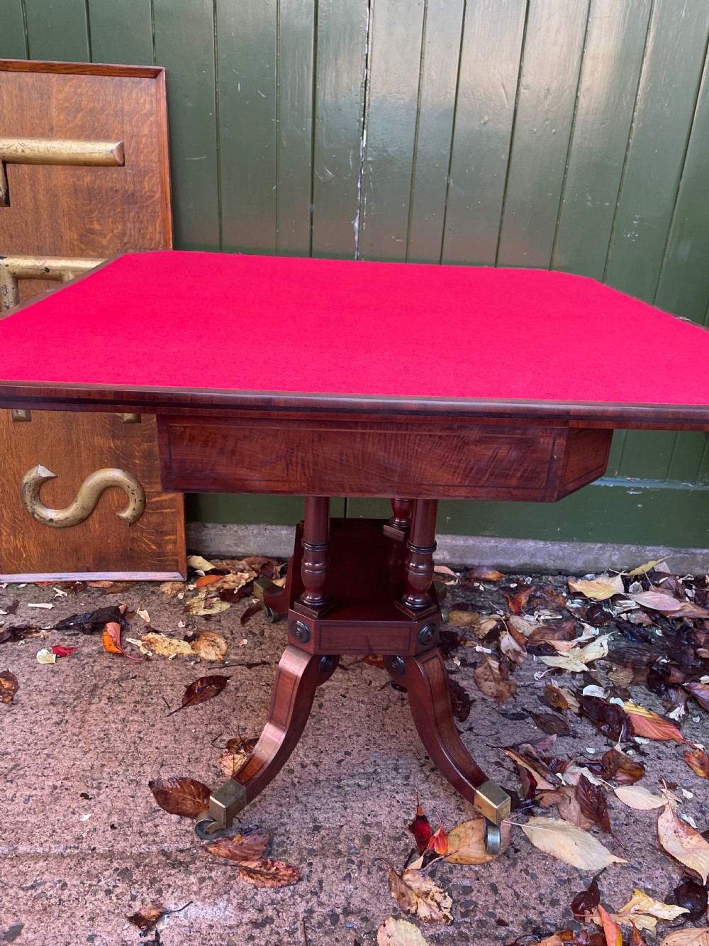 An early 19th-century Regency mahogany fold-over card table featuring turned column supports, a square platform base, and four splayed sabre legs with brass castors. View VI