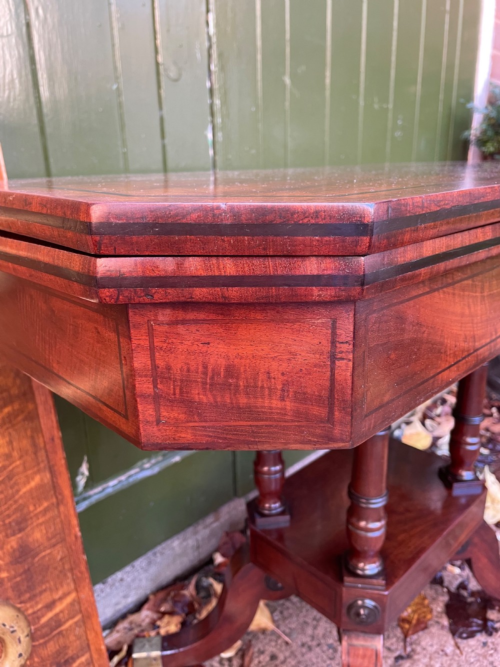 An early 19th-century Regency mahogany fold-over card table featuring turned column supports, a square platform base, and four splayed sabre legs with brass castors. View VII