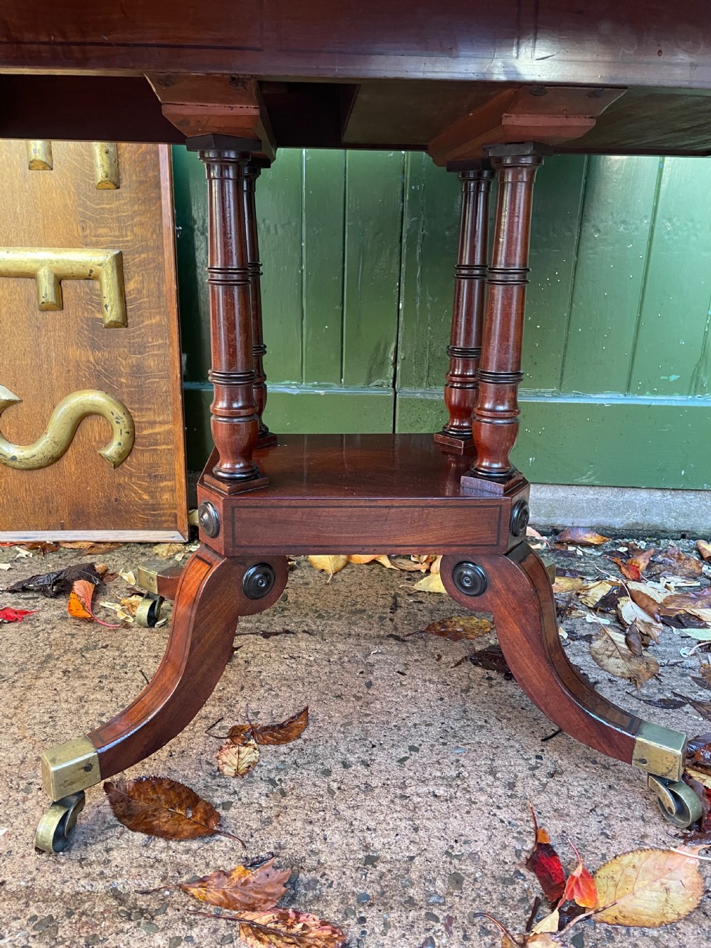 An early 19th-century Regency mahogany fold-over card table featuring turned column supports, a square platform base, and four splayed sabre legs with brass castors. View IX