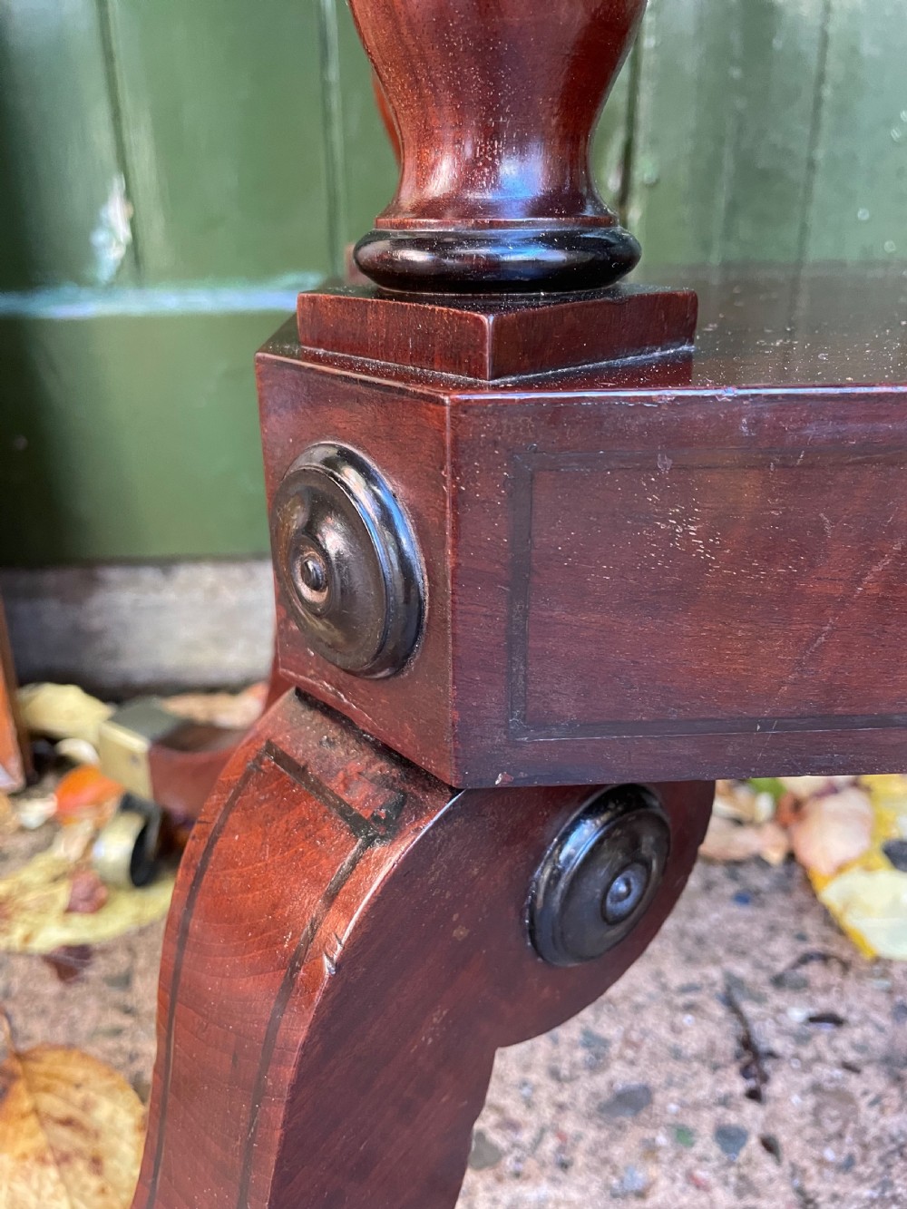 An early 19th-century Regency mahogany fold-over card table featuring turned column supports, a square platform base, and four splayed sabre legs with brass castors. View X