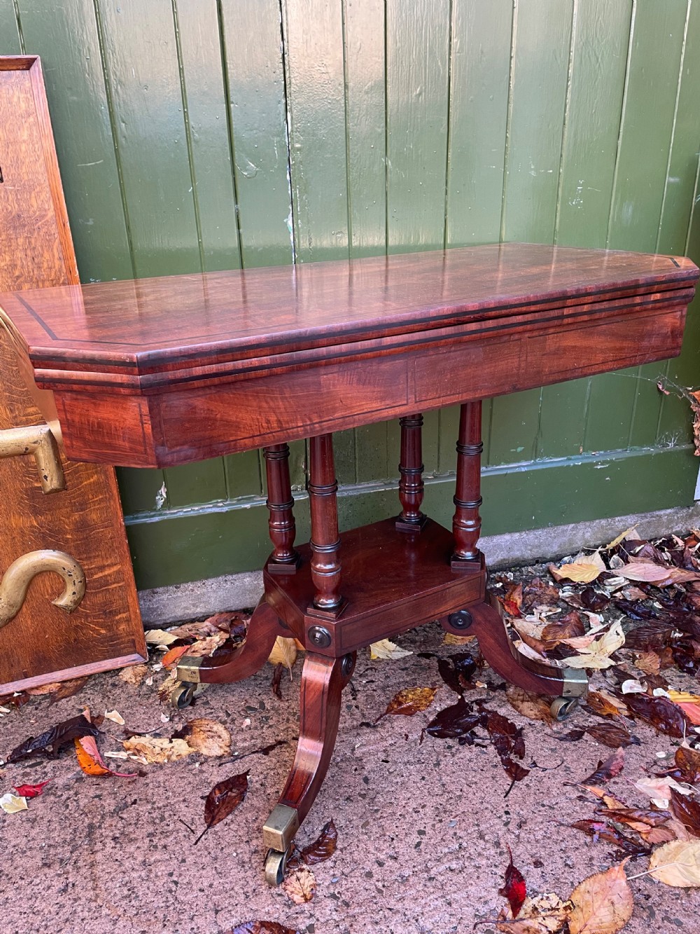 An early 19th-century Regency mahogany fold-over card table featuring turned column supports, a square platform base, and four splayed sabre legs with brass castors. View XII
