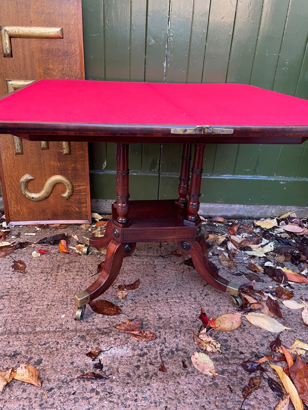 An early 19th-century Regency mahogany fold-over card table featuring turned column supports, a square platform base, and four splayed sabre legs with brass castors. View XIII