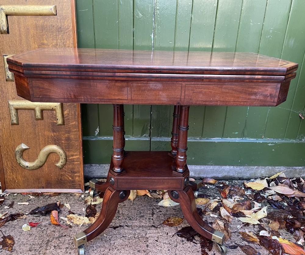 An early 19th-century Regency mahogany fold-over card table featuring turned column supports, a square platform base, and four splayed sabre legs with brass castors. View XVII