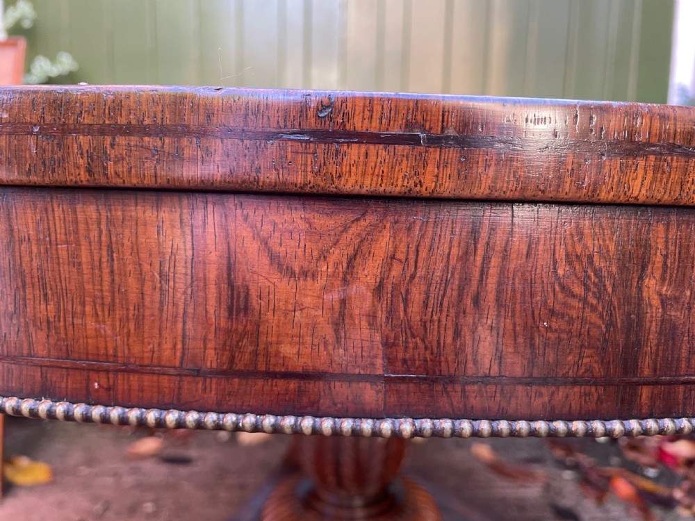 An early nineteenth-century circular Regency rosewood centre table featuring a crossbanded border, displayed in a tilted position on a pedestal base with castors. View VI
