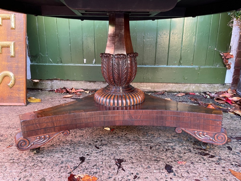 An early nineteenth-century circular Regency rosewood centre table featuring a crossbanded border, displayed in a tilted position on a pedestal base with castors. View VII