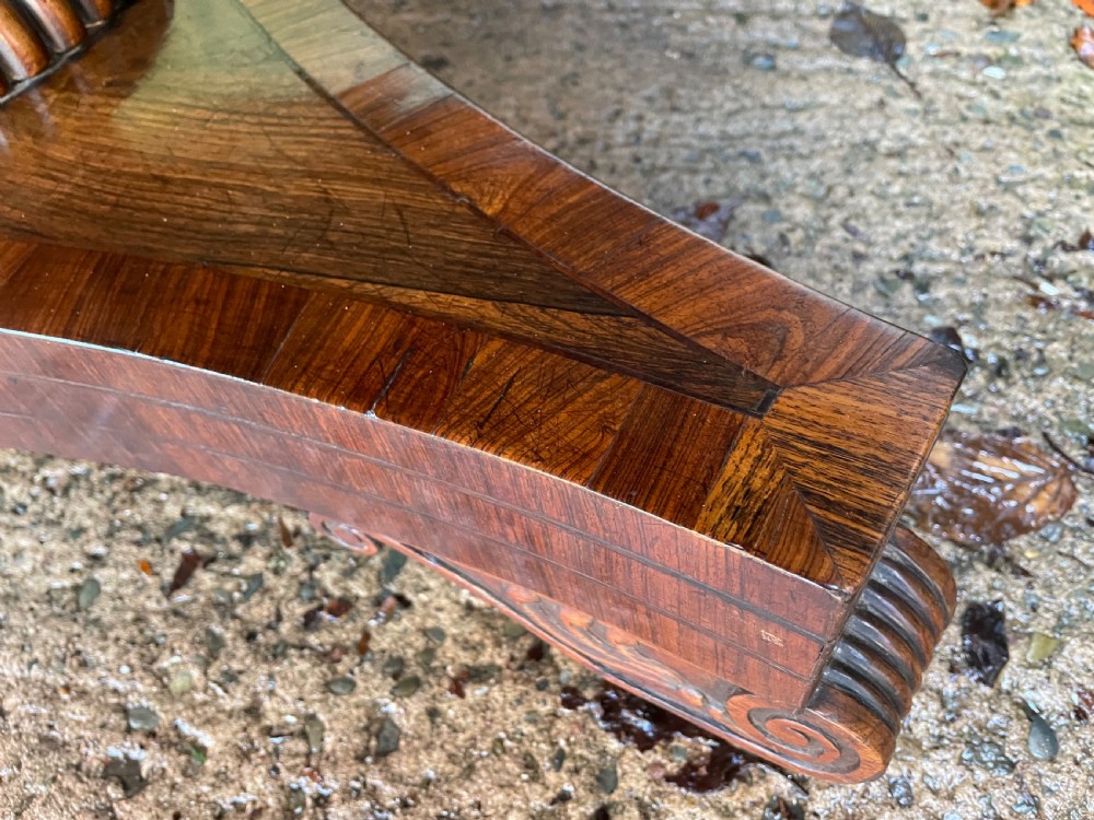 An early nineteenth-century circular Regency rosewood centre table featuring a crossbanded border, displayed in a tilted position on a pedestal base with castors. View X