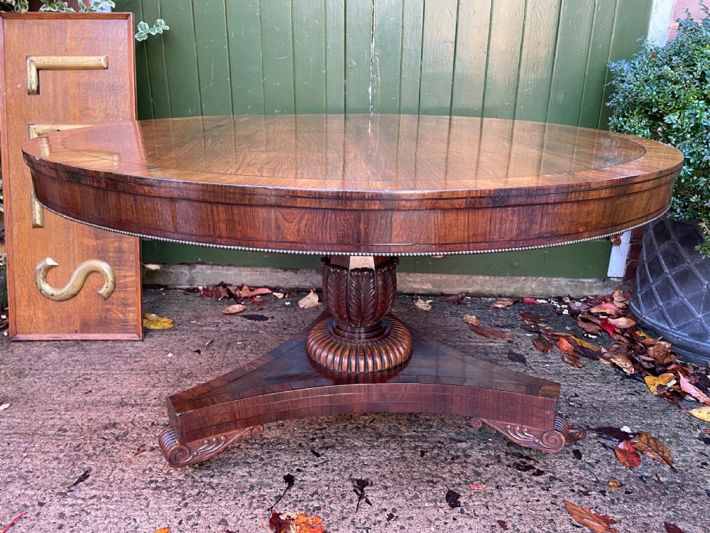 An early nineteenth-century circular Regency rosewood centre table featuring a crossbanded border, displayed in a tilted position on a pedestal base with castors. View XI