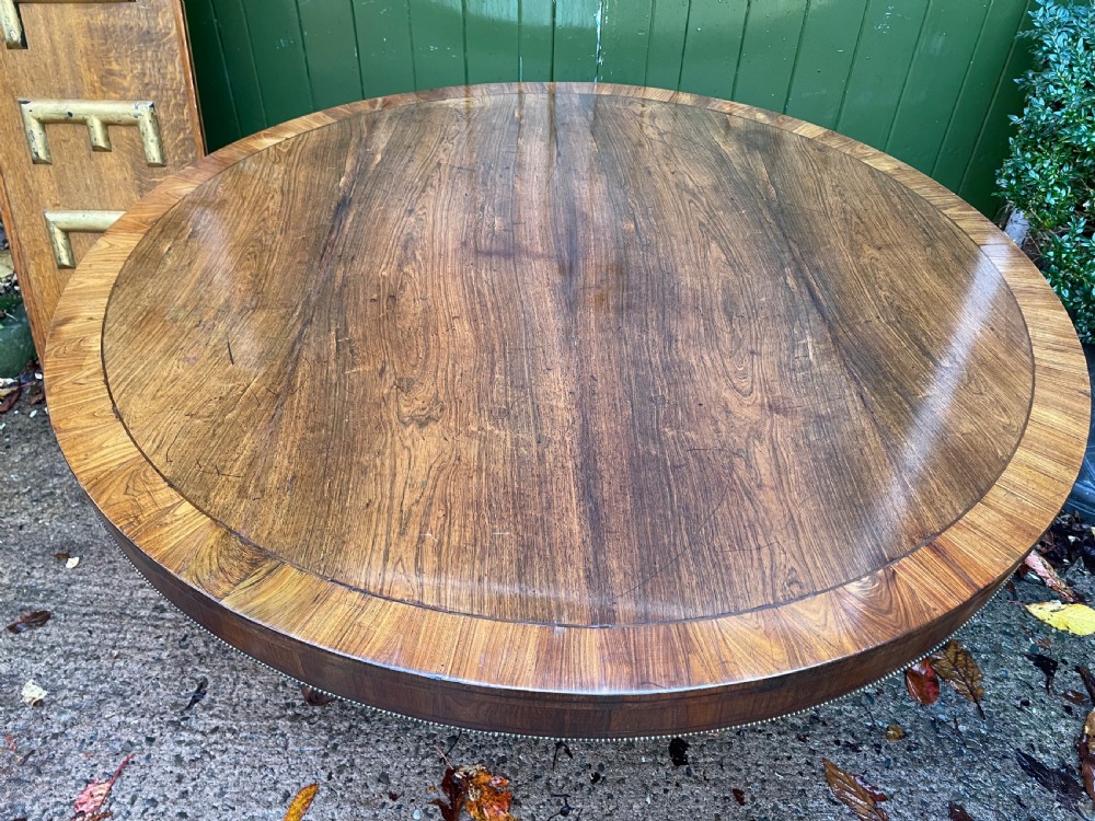 An early nineteenth-century circular Regency rosewood centre table featuring a crossbanded border, displayed in a tilted position on a pedestal base with castors. View XVI