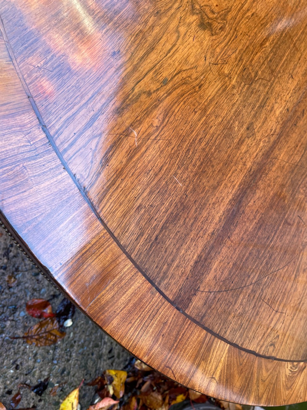 An early nineteenth-century circular Regency rosewood centre table featuring a crossbanded border, displayed in a tilted position on a pedestal base with castors. View XVIII