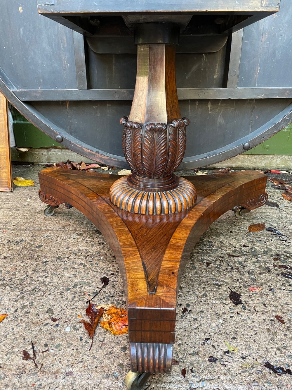 An early nineteenth-century circular Regency rosewood centre table featuring a crossbanded border, displayed in a tilted position on a pedestal base with castors. View XX
