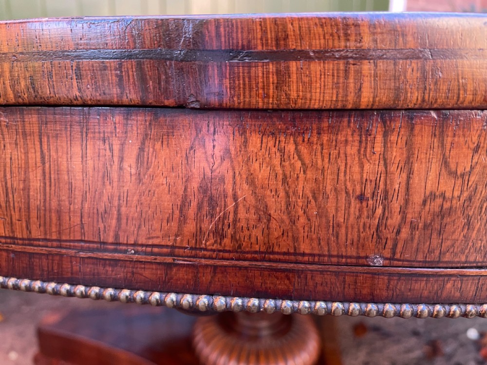 An early nineteenth-century circular Regency rosewood centre table featuring a crossbanded border, displayed in a tilted position on a pedestal base with castors. View XXII