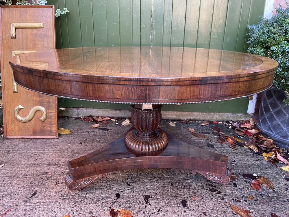 An early nineteenth-century circular Regency rosewood centre table featuring a crossbanded border, displayed in a tilted position on a pedestal base with castors. View V