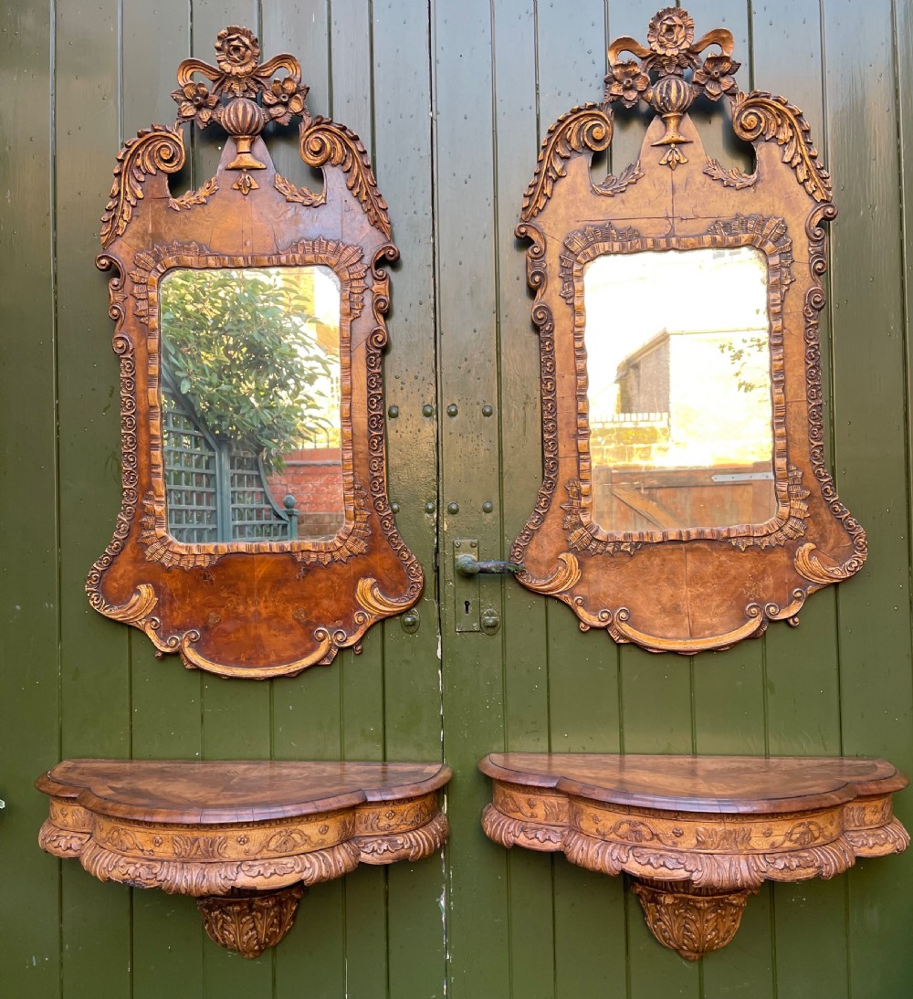 A pair of late nineteenth century carved walnut and parcel-gilt wall consoles with matching arch-top mirrors featuring urn and floral cresting.