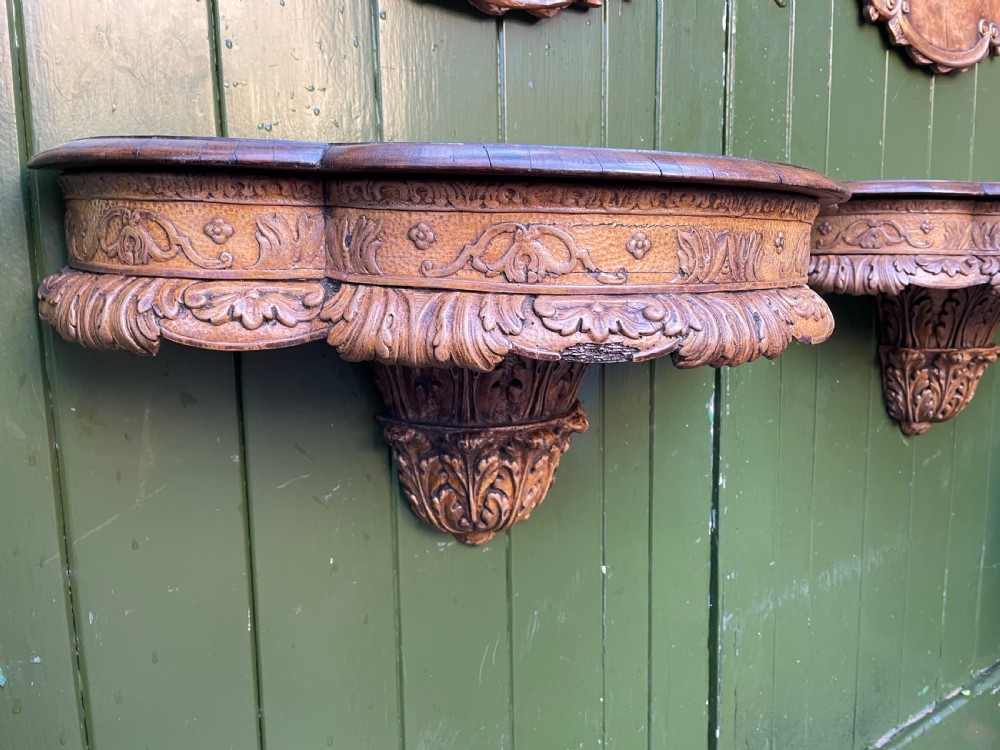 A pair of late nineteenth century carved walnut and parcel-gilt wall consoles with matching arch-top mirrors featuring urn and floral cresting. View XIX