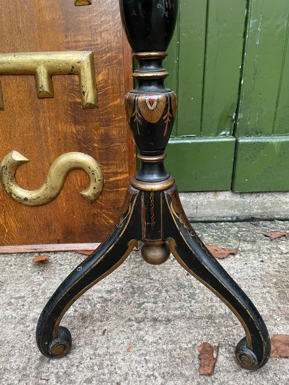 A black lacquered wooden torchere stand featuring gilt floral chinoiserie decoration, a turned central shaft, and a tripod base. View V