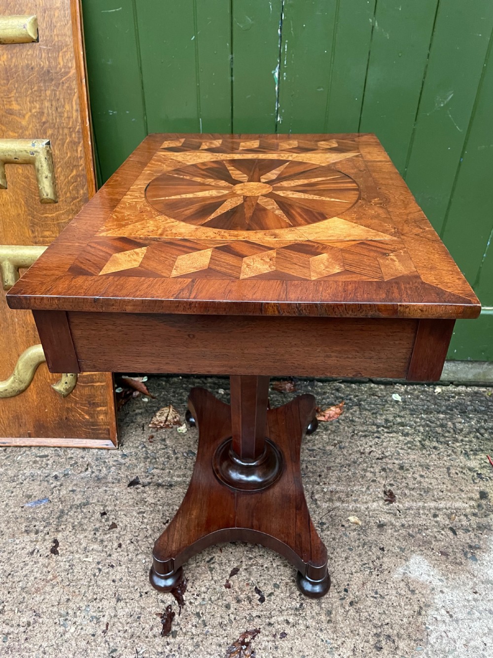 A nineteenth-century rectangular rosewood side table featuring a starburst specimen wood inlaid top set on a pedestal base with a quadform platform. View VI