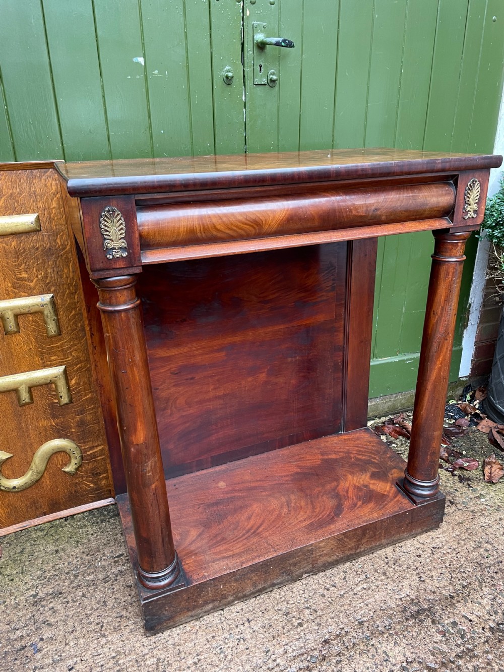 Early 19th-century George IV mahogany console table featuring cylindrical front columns, brass mounts, a plinth base, and a flame mahogany backdrop. View II