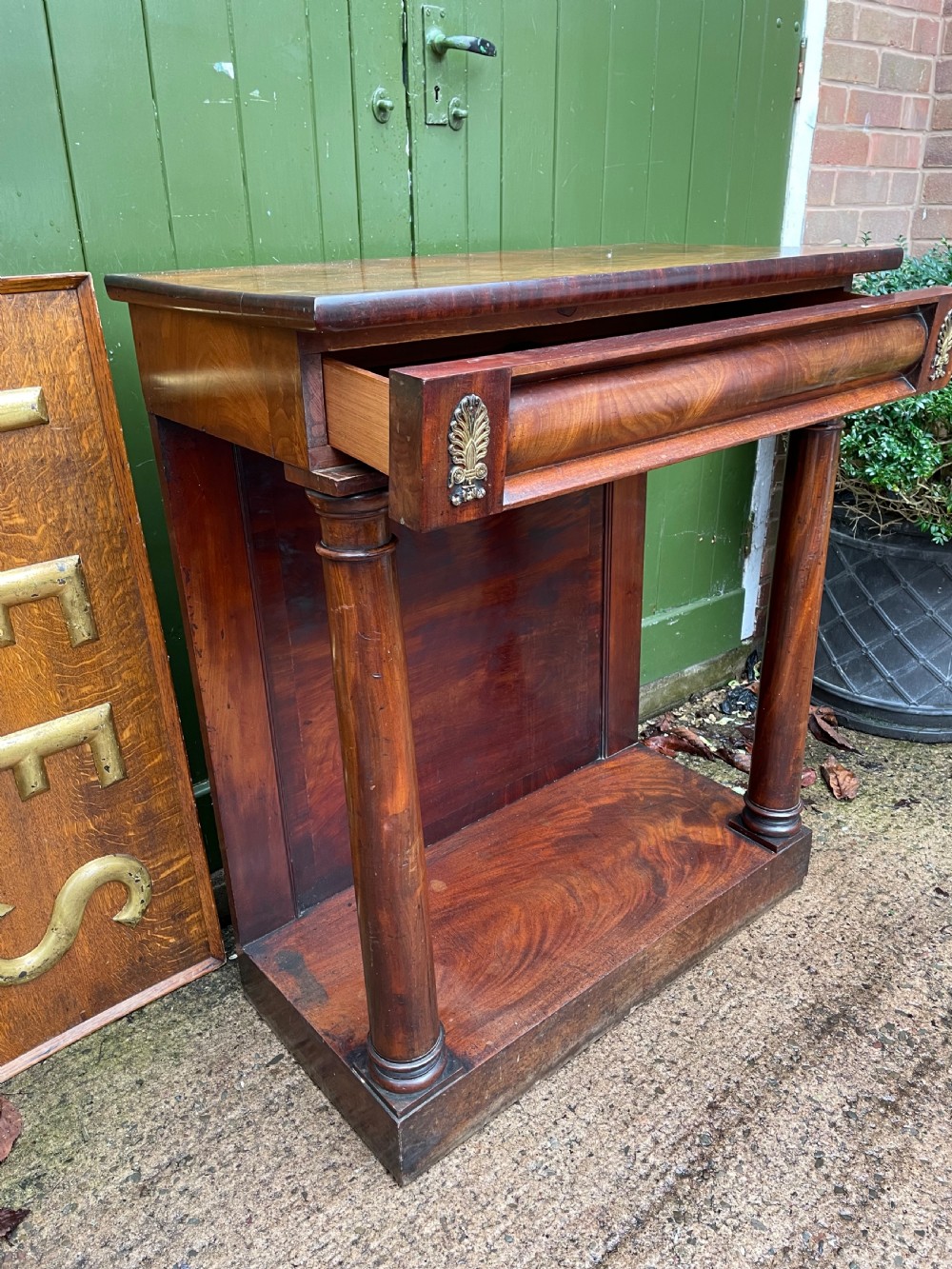 Early 19th-century George IV mahogany console table featuring cylindrical front columns, brass mounts, a plinth base, and a flame mahogany backdrop. View III