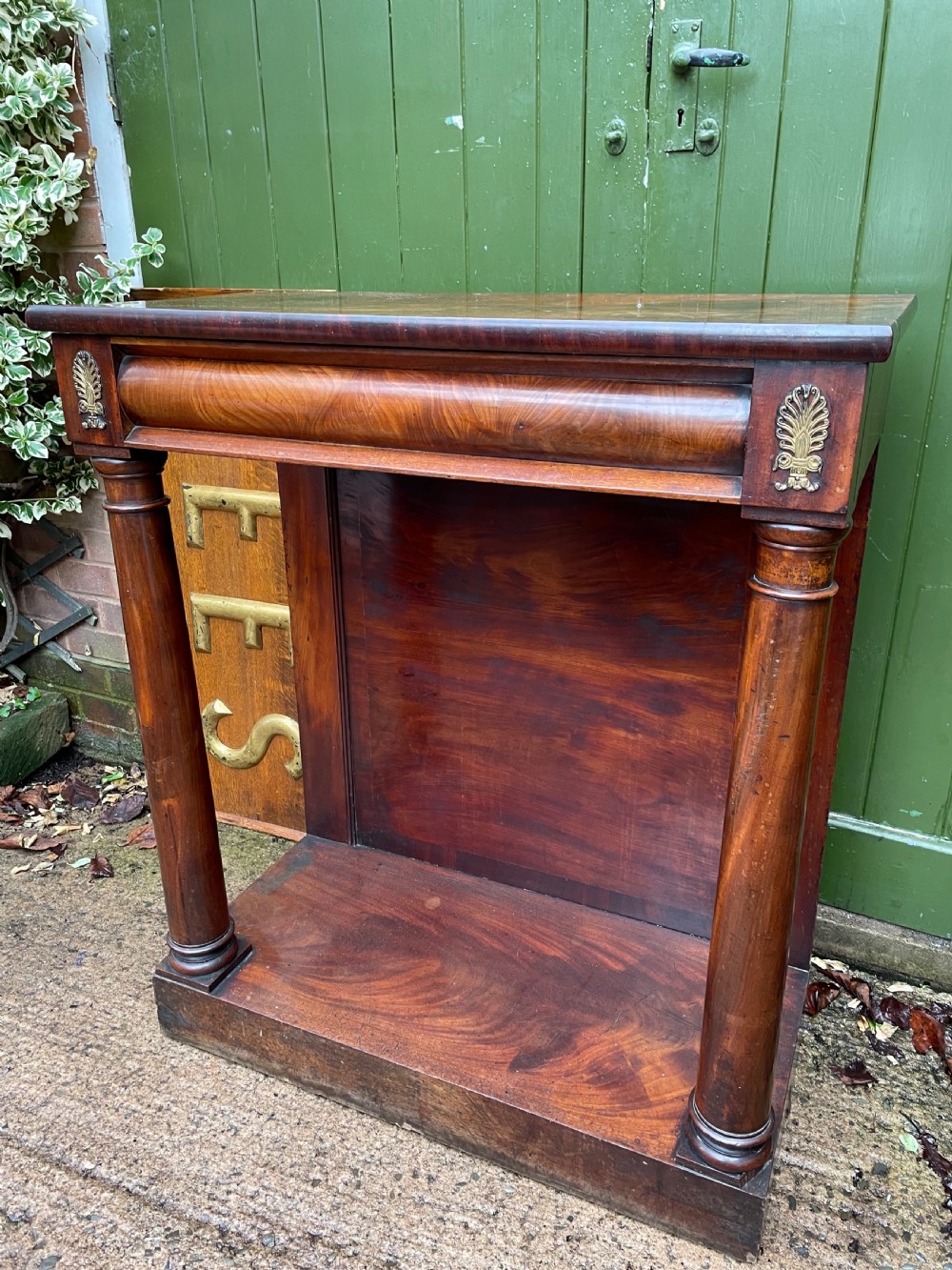 Early 19th-century George IV mahogany console table featuring cylindrical front columns, brass mounts, a plinth base, and a flame mahogany backdrop. View VI