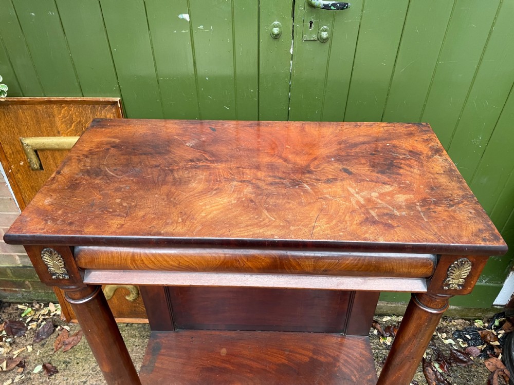 Early 19th-century George IV mahogany console table featuring cylindrical front columns, brass mounts, a plinth base, and a flame mahogany backdrop. View VII