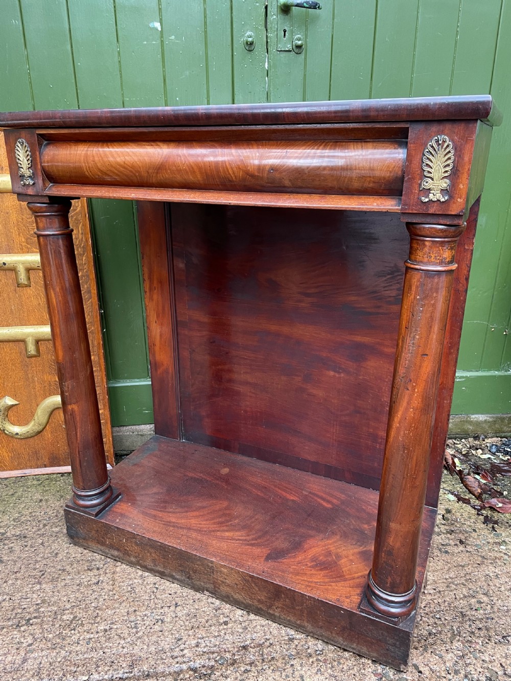 Early 19th-century George IV mahogany console table featuring cylindrical front columns, brass mounts, a plinth base, and a flame mahogany backdrop. View IX