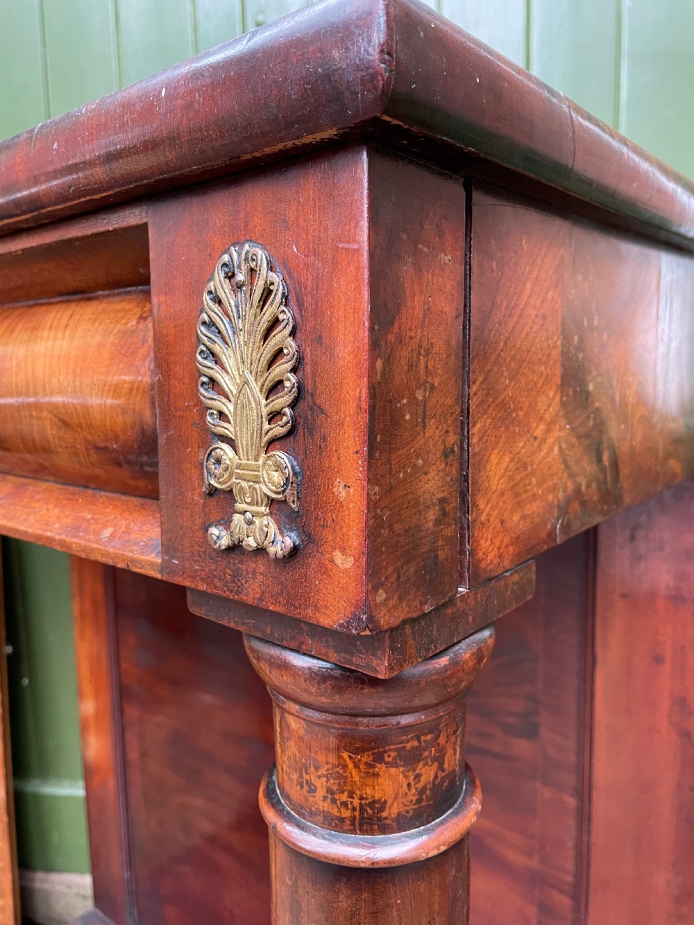 Early 19th-century George IV mahogany console table featuring cylindrical front columns, brass mounts, a plinth base, and a flame mahogany backdrop. View X