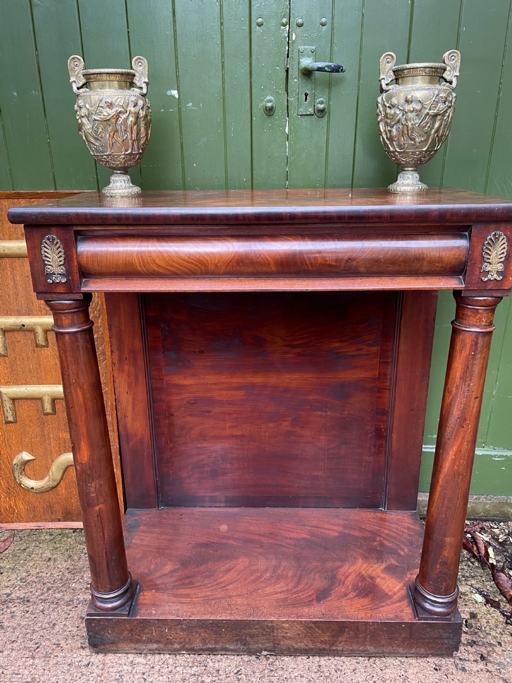 Early 19th-century George IV mahogany console table featuring cylindrical front columns, brass mounts, a plinth base, and a flame mahogany backdrop. View XIV