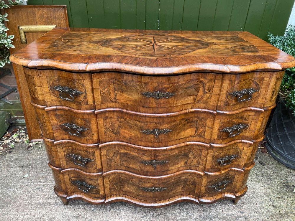 A mid-18th-century German Baroque walnut commode featuring a shaped serpentine front, four long drawers with figured wood veneers, and ornate cast brass handles. View II