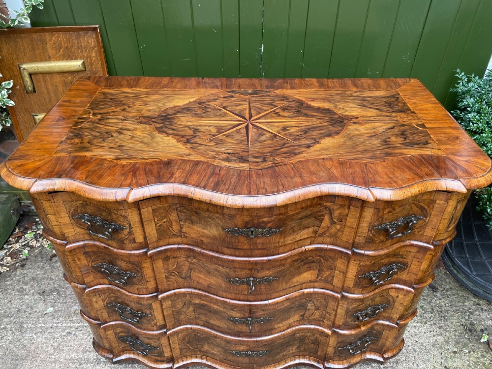 A mid-18th-century German Baroque walnut commode featuring a shaped serpentine front, four long drawers with figured wood veneers, and ornate cast brass handles. View V
