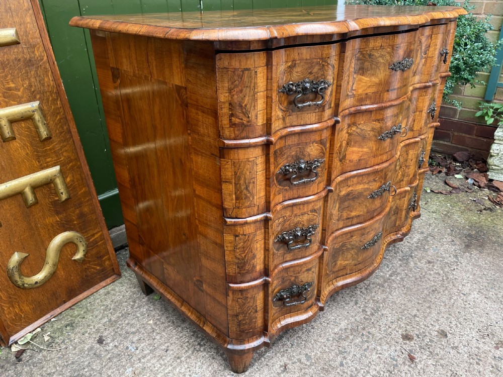 A mid-18th-century German Baroque walnut commode featuring a shaped serpentine front, four long drawers with figured wood veneers, and ornate cast brass handles. View VI